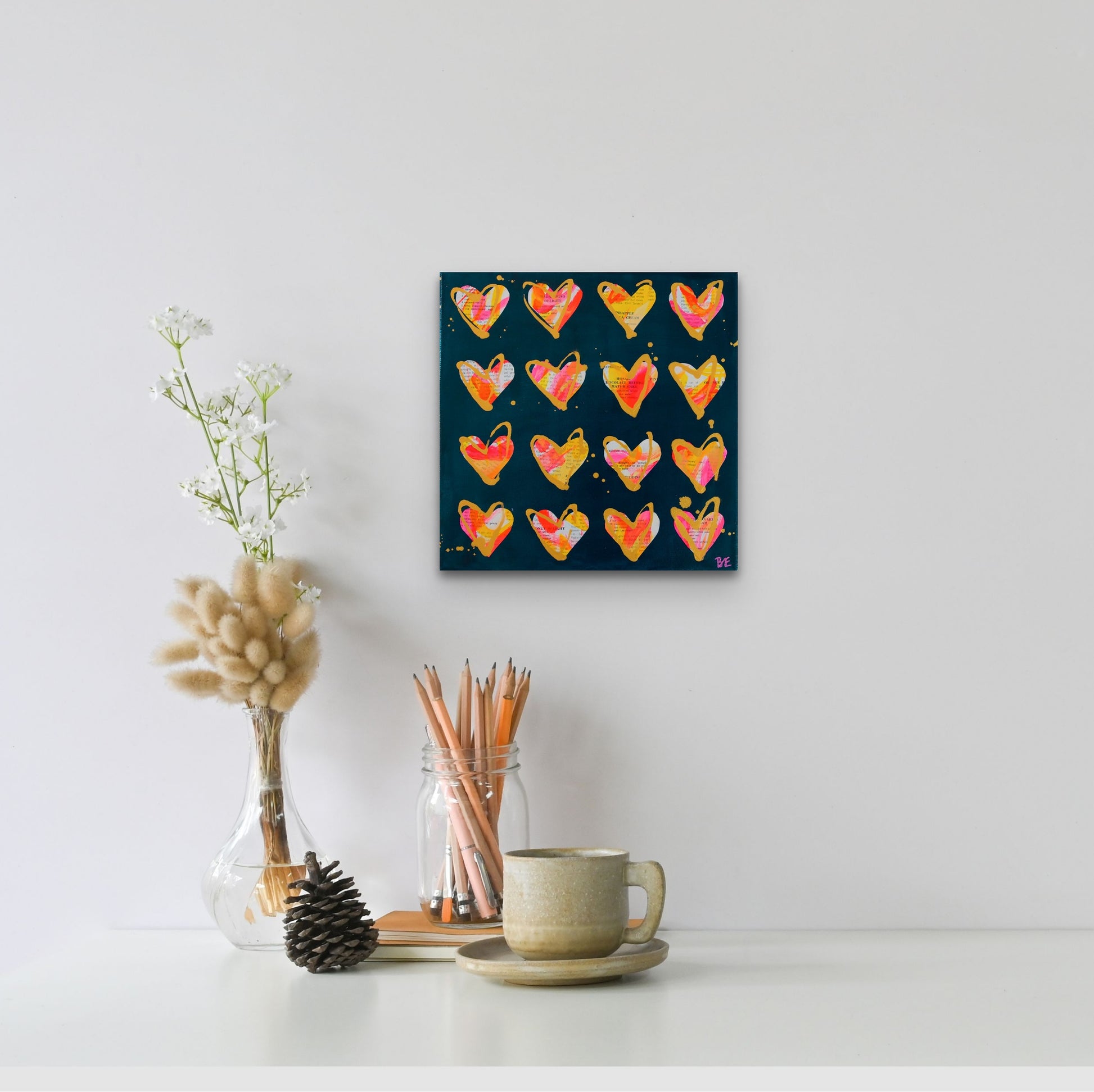 Maraschino Delight: Original Mixed Media Artwork with Vintage Cookbook and Hearts from Bridget Edwards Studio hangs on white wall behind coffee cup and jar of pencils